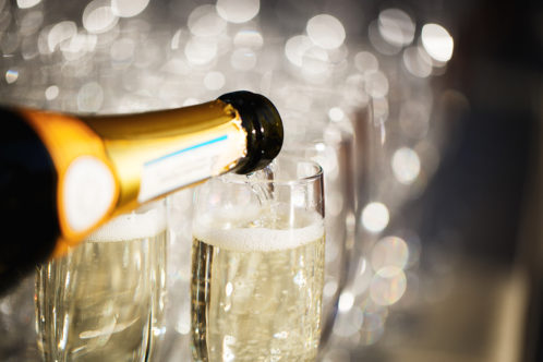 close up of a bottle pouring champagne into glasses with blurred background