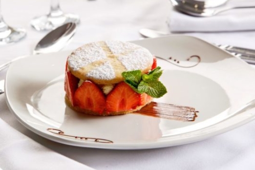 Strawberry dessert on white plate on a white table with a glass of red wine