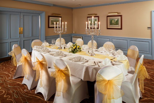 The Gillian Suite at Mercure Livingston Hotel, set up for a wedding breakfast, pretty blue painted wood panelling, yellow sashes, white linen, silver candlestick