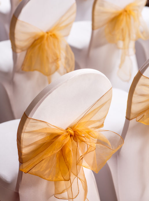 Close up of chairs set up for wedding ceremony, white linen, yellow sashes